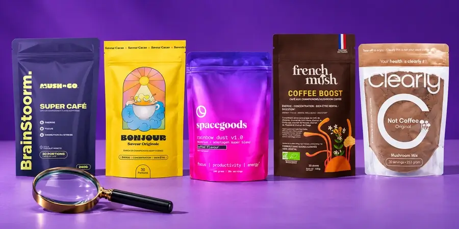 Bolsas de Brainstoorm, Bonjour Drink, Spacegoods Rainbow Dust, Coffee Boost de French Mush y Clearly Not Coffee sobre una mesa, con una lupa delante de la bolsa de Brainstoorm