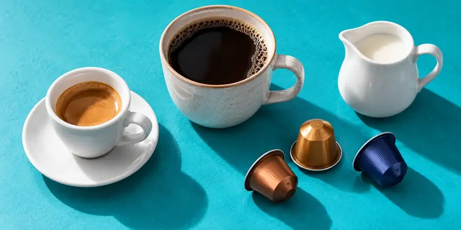 Taza de expreso, taza de café de filtro, cápsulas de café y una jarrita de leche